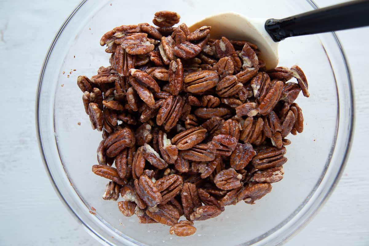 pecans coated with egg white in a glass bowl.