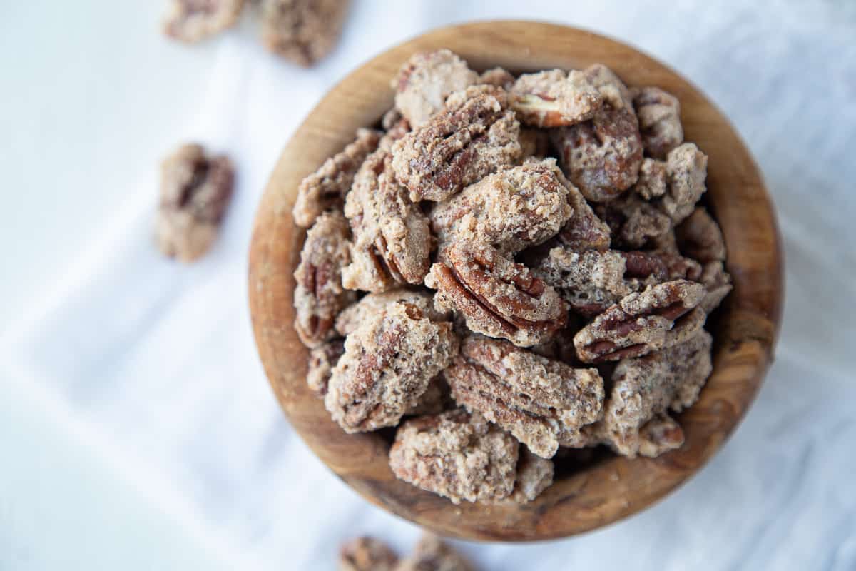 cinnamon roasted nuts in a wooden bowl on a white tea towel.