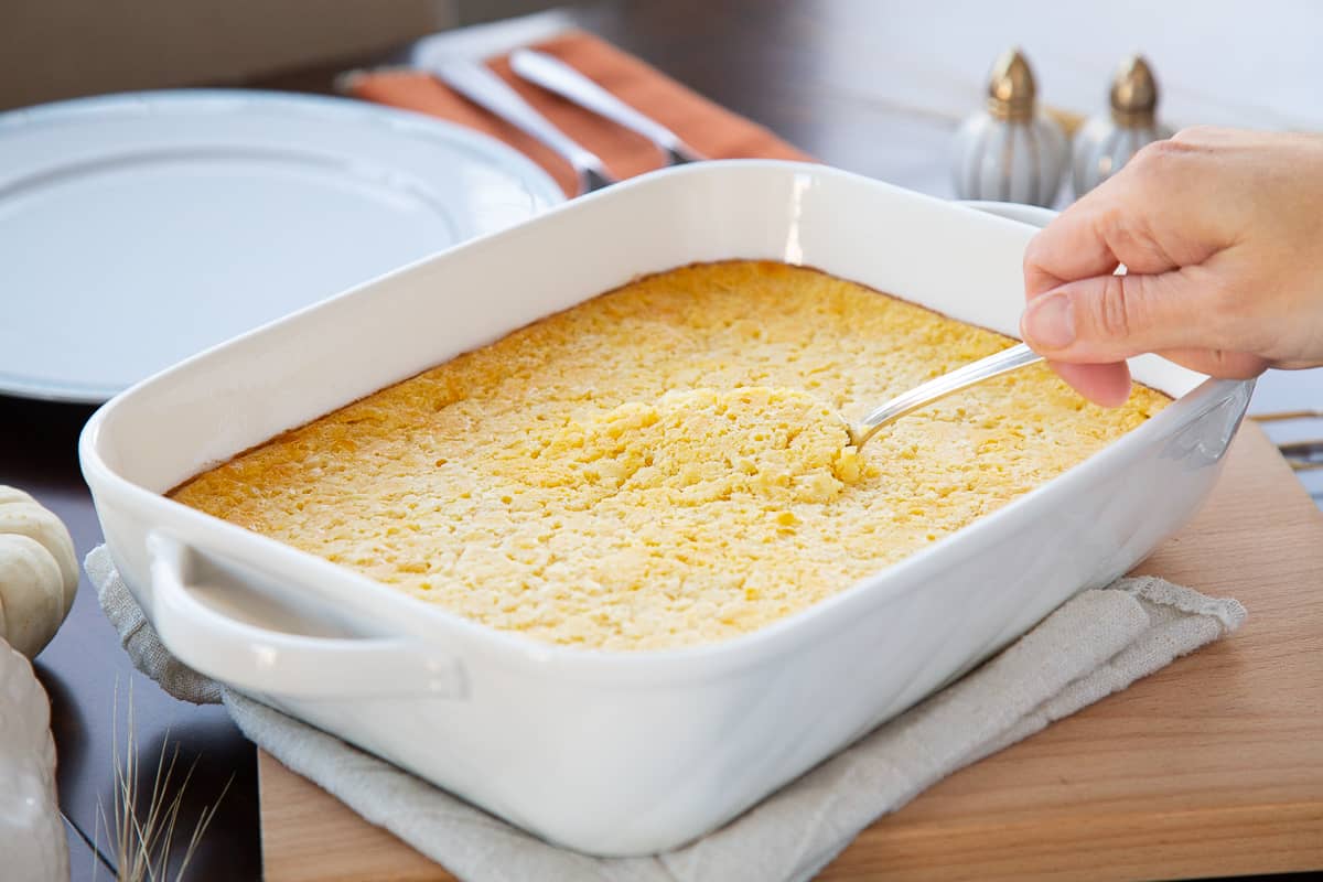 spoon lifting a piece of corn casserole out of a white casserole dish.