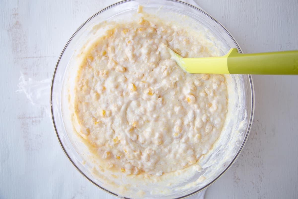 batter for corn casserole in a glass bowl with a yellow and green spatula.