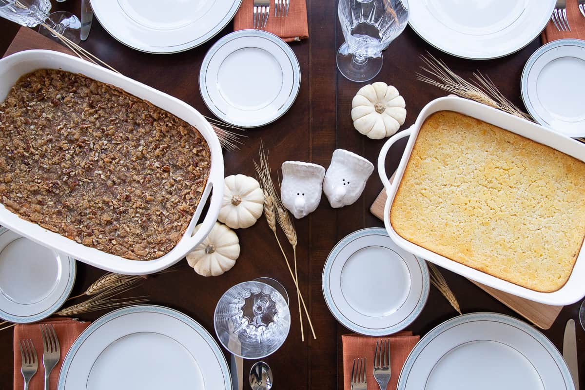 table set for thanksgiving with corn casserole, sweet potato casserole, plates, and white mini pumpkins.