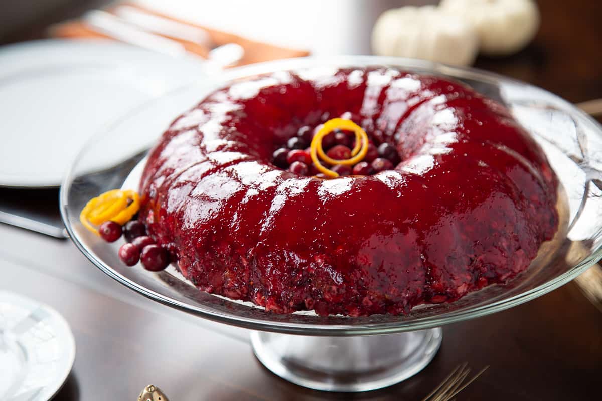 cranberry jello salad on a glass cake stand on a wooden table.