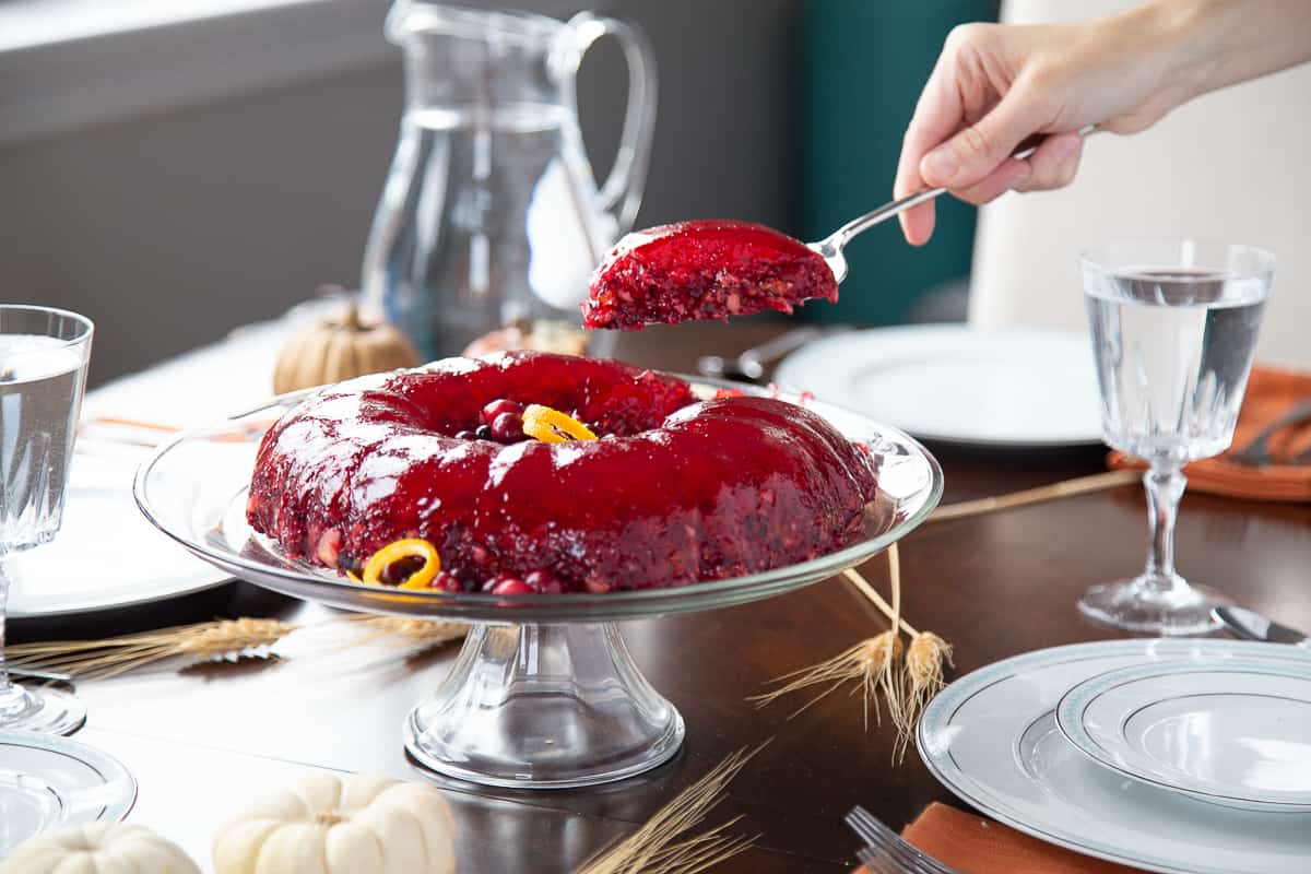 hand lifting a piece of cranberry jello salad off of a serving platter.