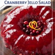 cranberry jello salad on a glass platter garnished with fresh cranberries and orange peel.