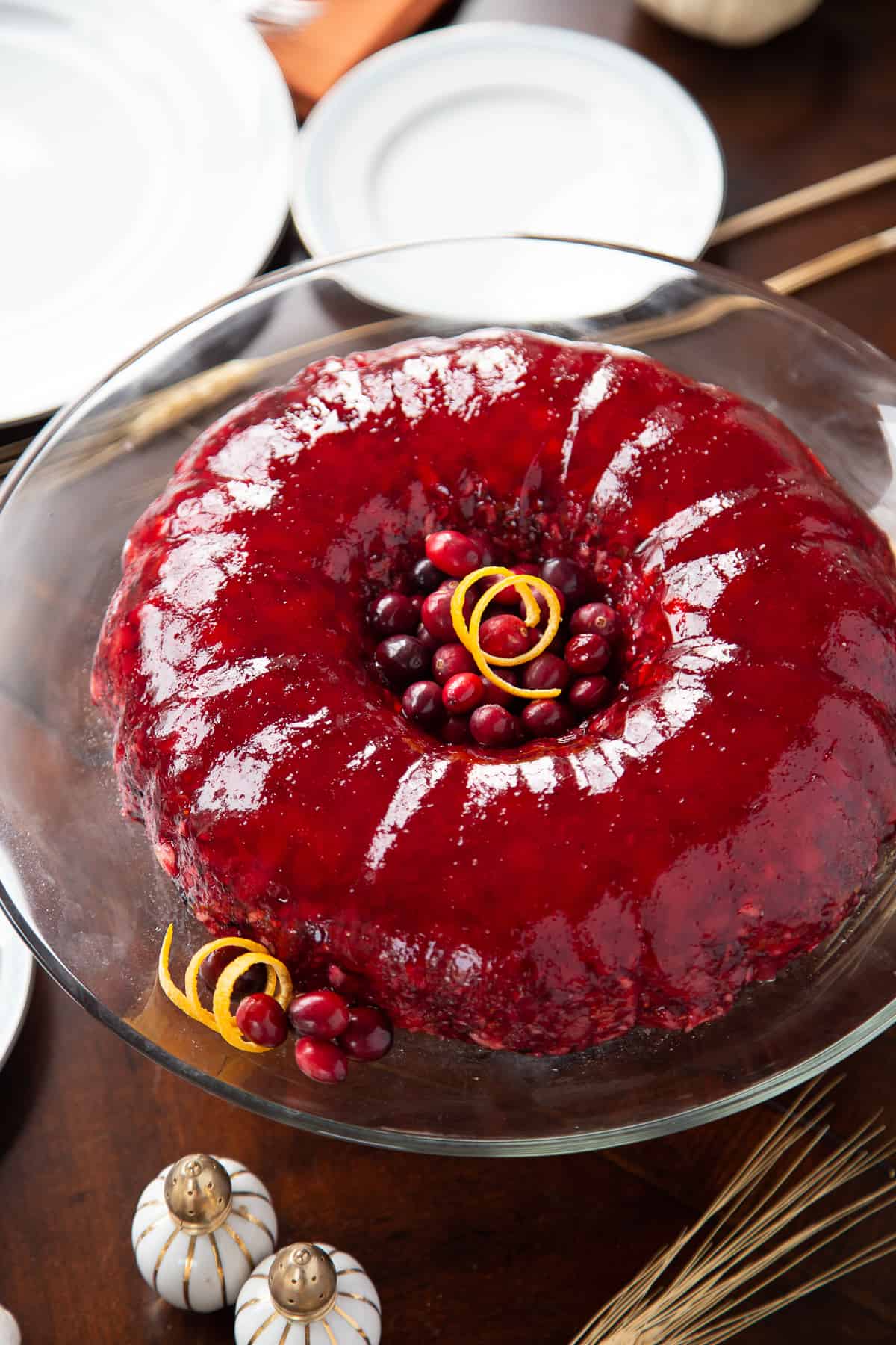 ring of cranberry jello salad on a glass cake stand on a wooden dinner table.