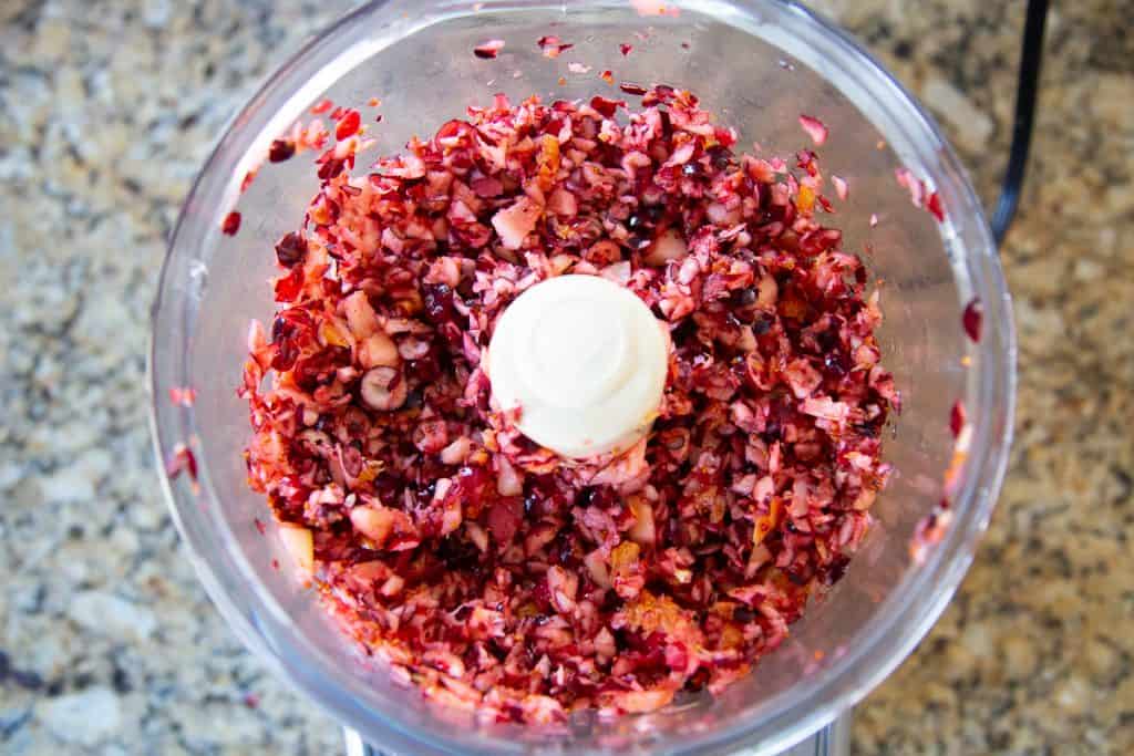 shredded cranberries and fruit in the bowl of a food processor.