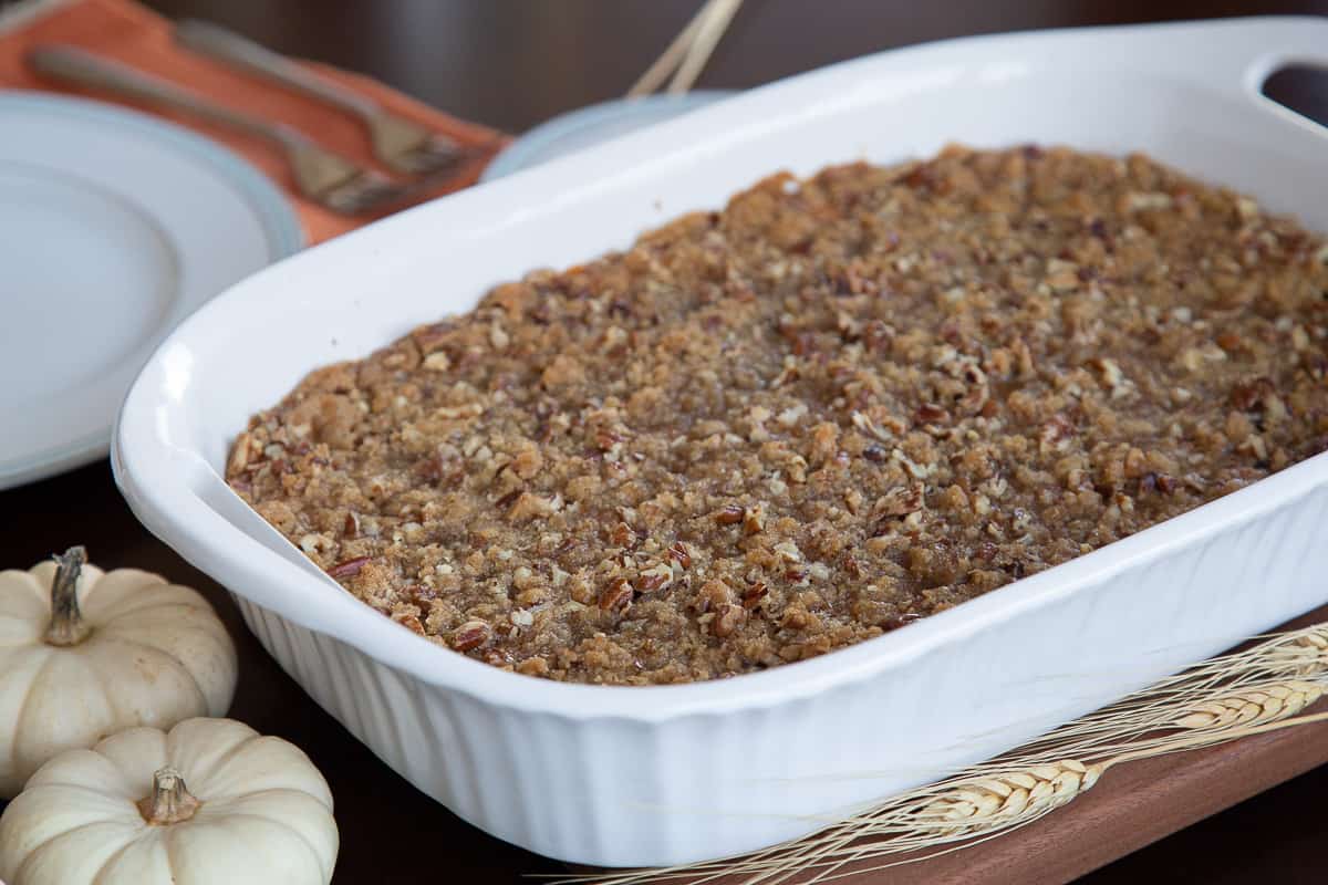 sweet potato casserole with pecan topping in a white casserole dish next to two mini white pumpkins.