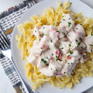 turkey a la king on egg noodles on a white plate on top of a colorful napkin.