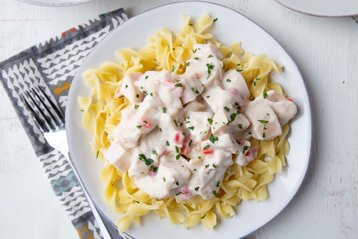 turkey a la king over egg noodles on a white plate on a dinner table.