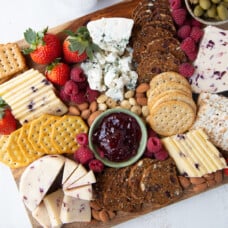 cheese, crackers, jam, and fruit on a rectangular wooden board.