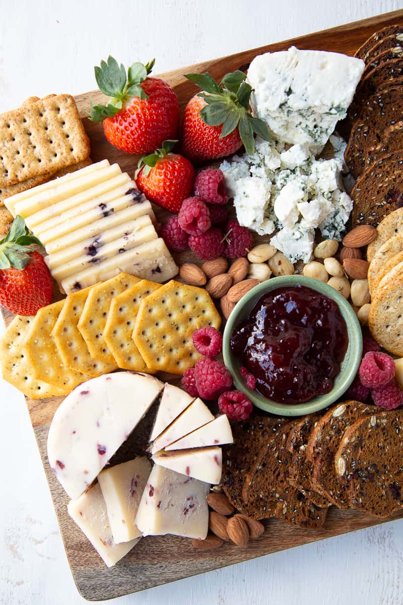 cheese, crackers, fruit, and jam on a wooden board.