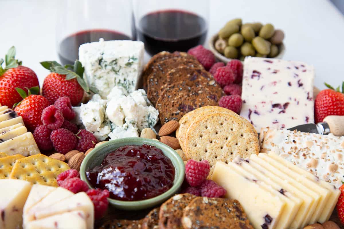 jam, olives, cheese, and crackers with a glass of wine in the background.