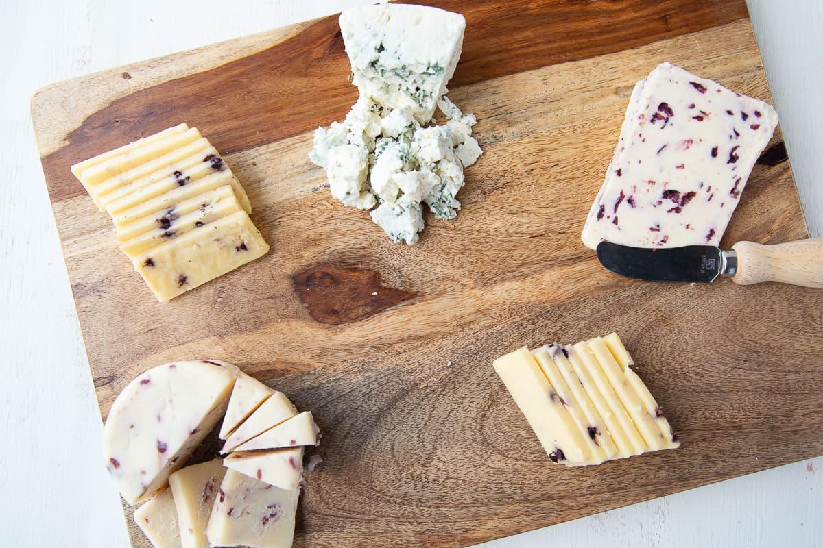 five types of cheeses on a wooden board.