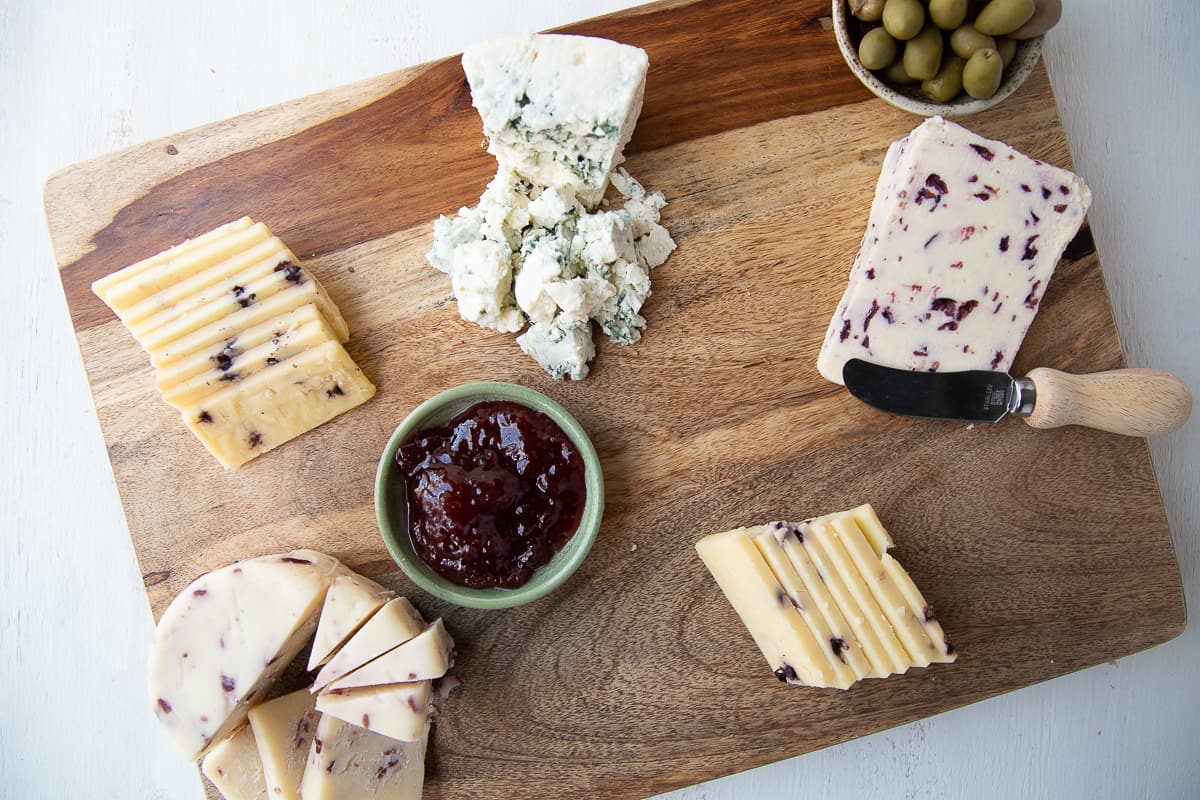 cheese, olives, and jam on a wooden board.