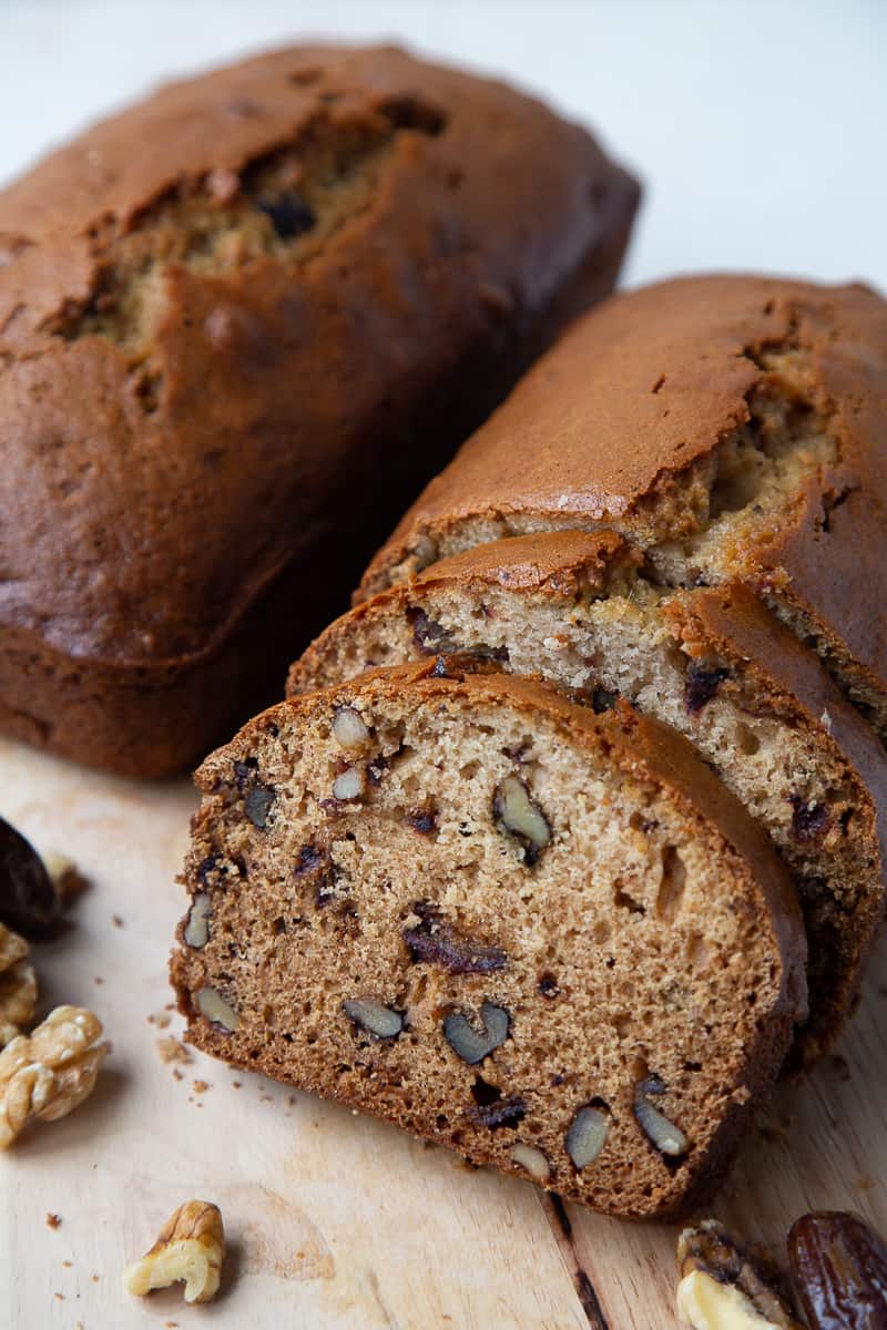 two loaves of a brown bread with dates and nuts, with a slice cut out.