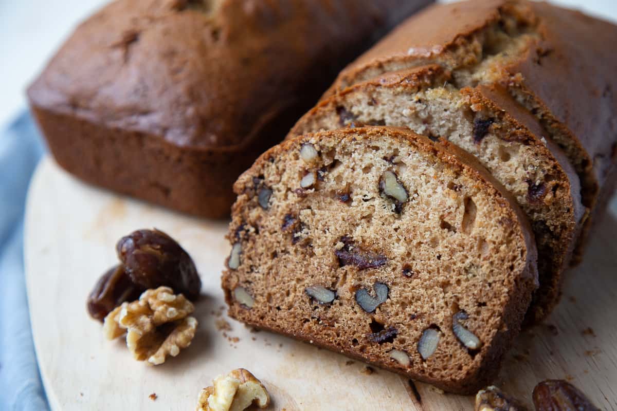 date nut bread on a wooden board with dates and walnuts on the side.