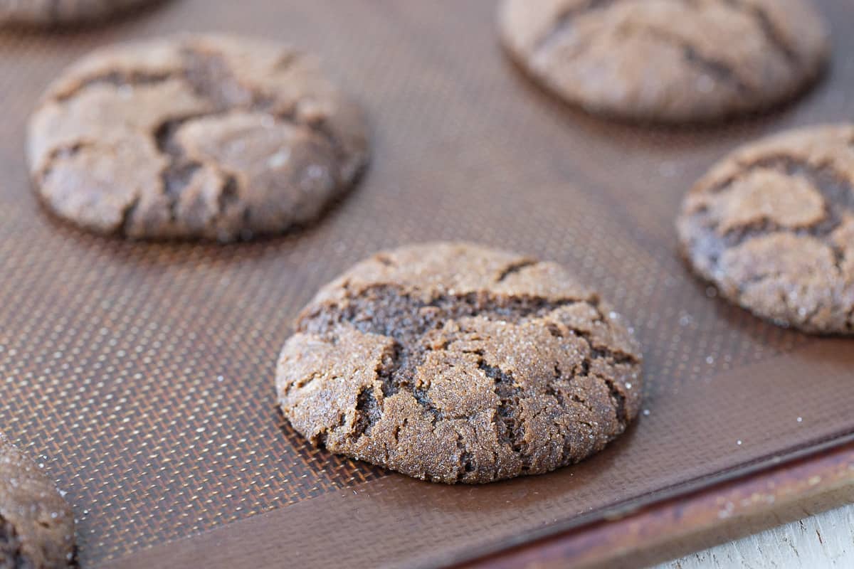 baked ginger cookies with cracks on a baking sheet.