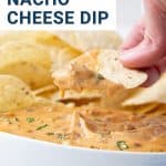 hand scooping nacho cheese dip from a white bowl.