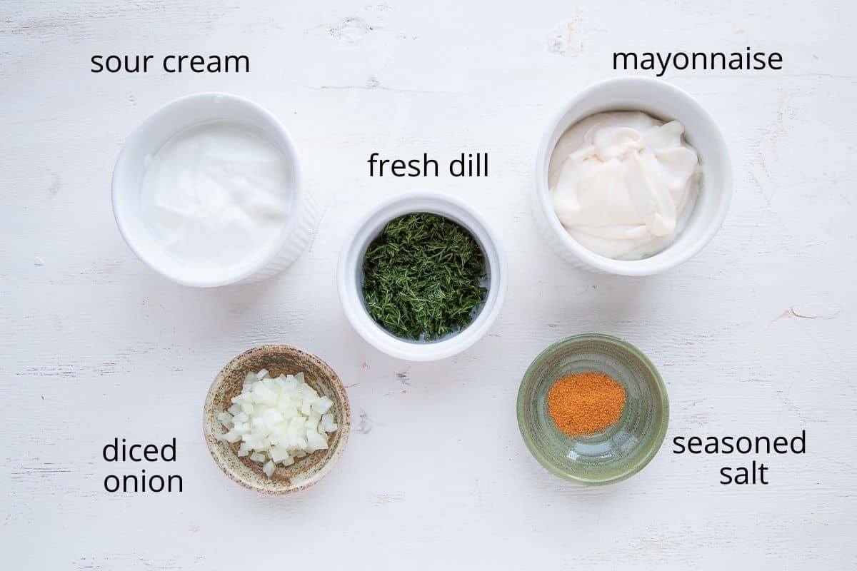 ramekins of sour cream, mayo, dill, onion, and seasoned salt on a white table.