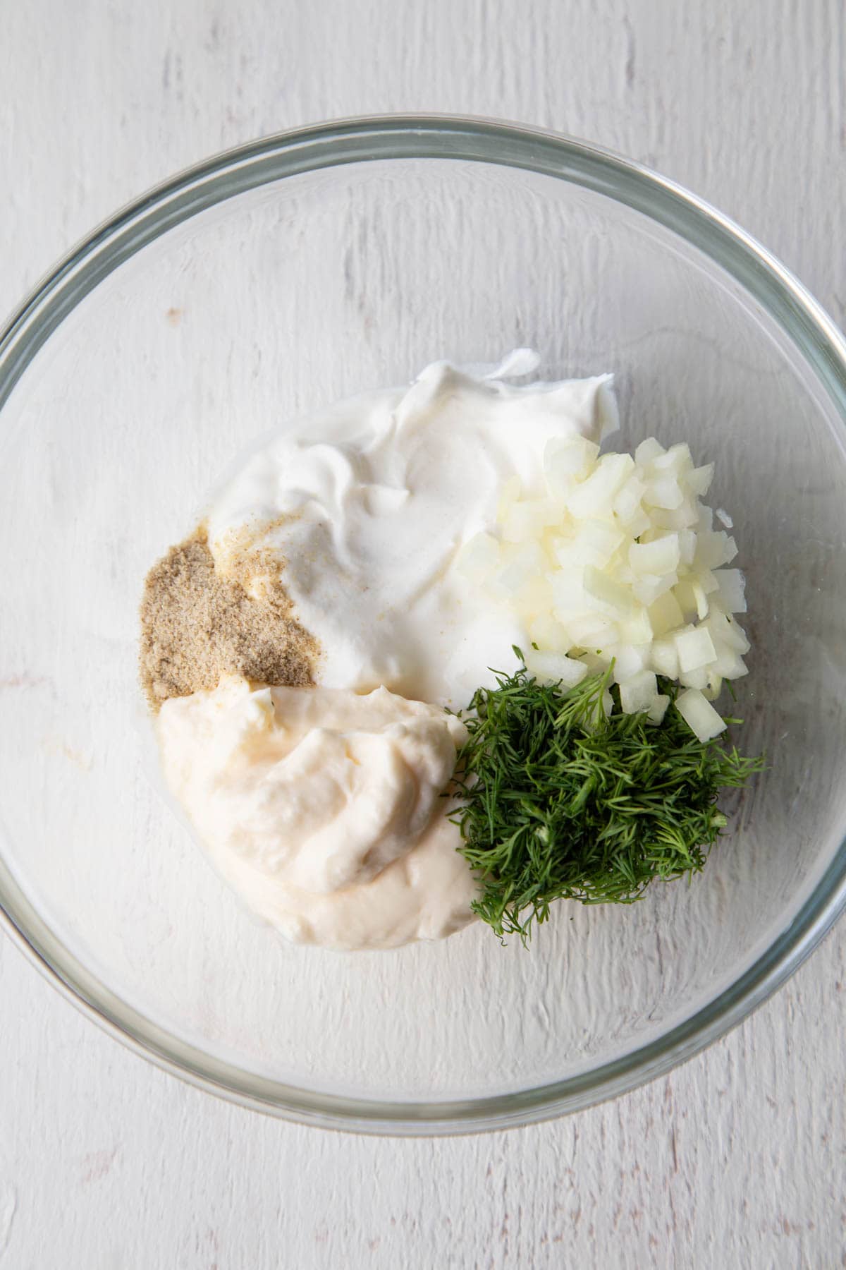 sour cream, mayo, dill, beau monde seasoning, and onion in a bowl.