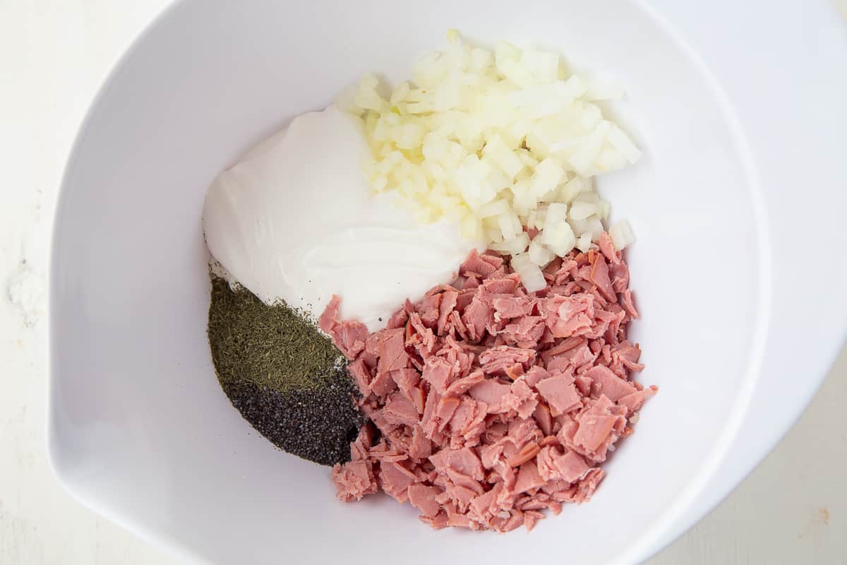 sour cream, chopped onion, deli beef, and other ingredients in a white bowl.