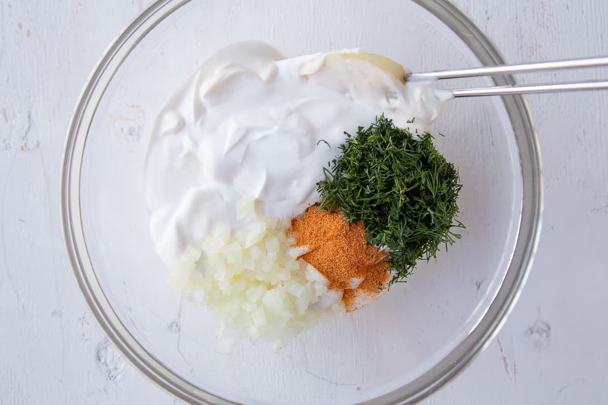 sour cream, mayo, dill, onion, and seasoned salt in a glass bowl with a spatula.