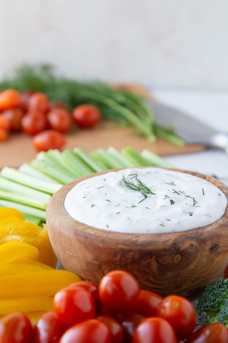sour cream dill dip in a wooden bowl surrounded by fresh vegetables.