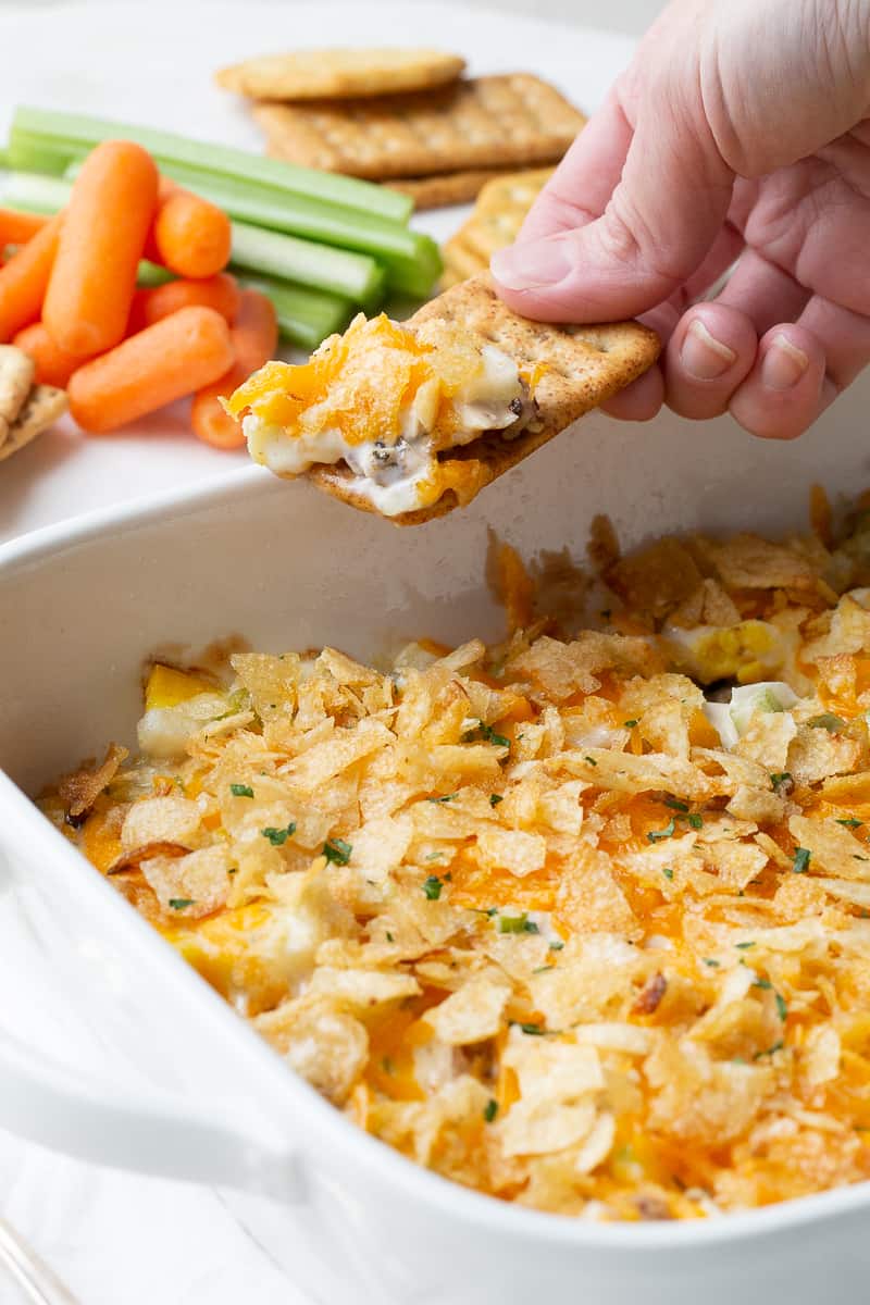 hand with a cracker scooping up hot chicken salad from a casserole dish.