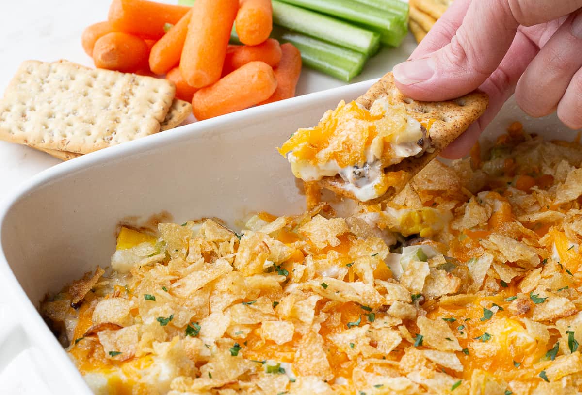 hand dipping a cracker into hot chicken salad.