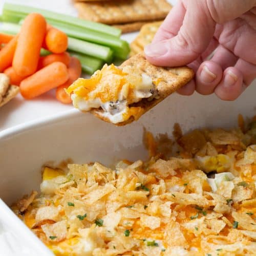 hand dipping a cracker into hot chicken salad.