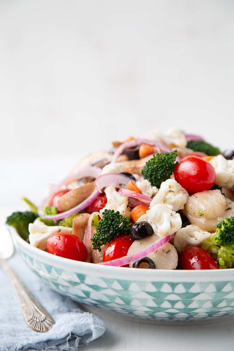 marinated vegetable salad in a green and white bowl next to a blue napkin.