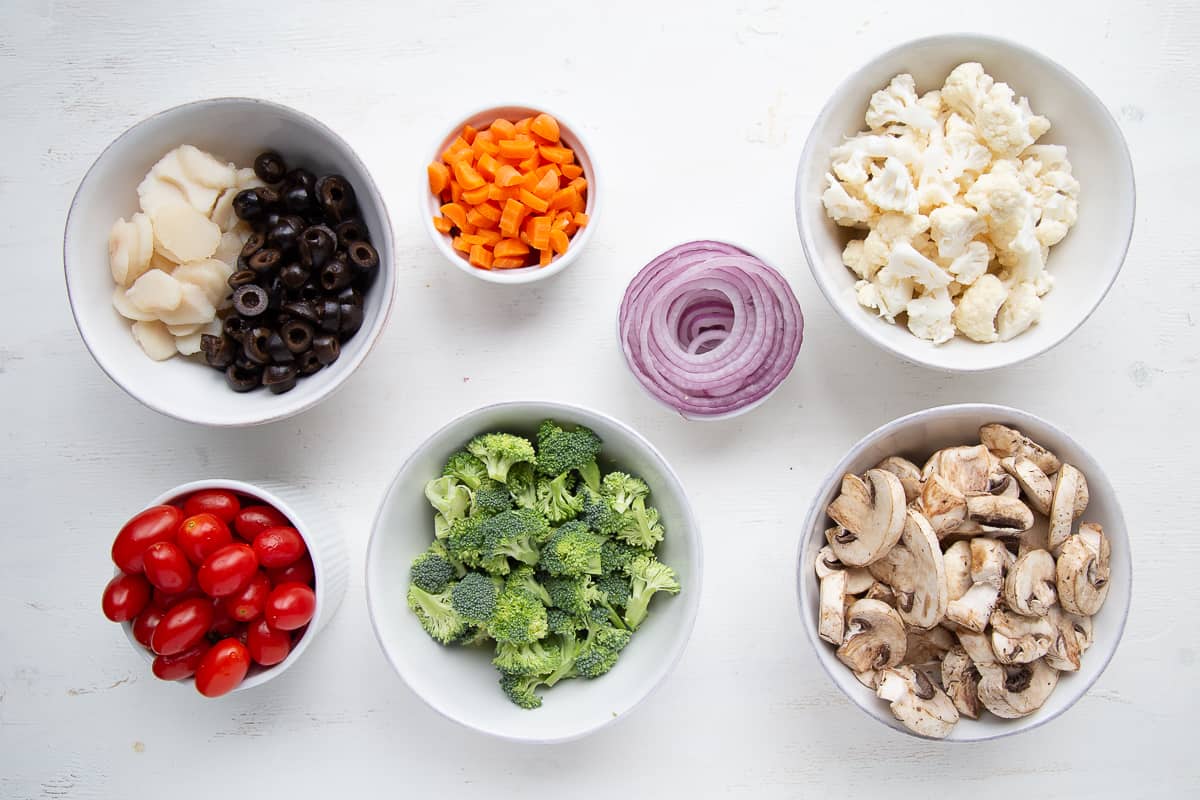 vegetable salad ingredients in small bowls on a white table.