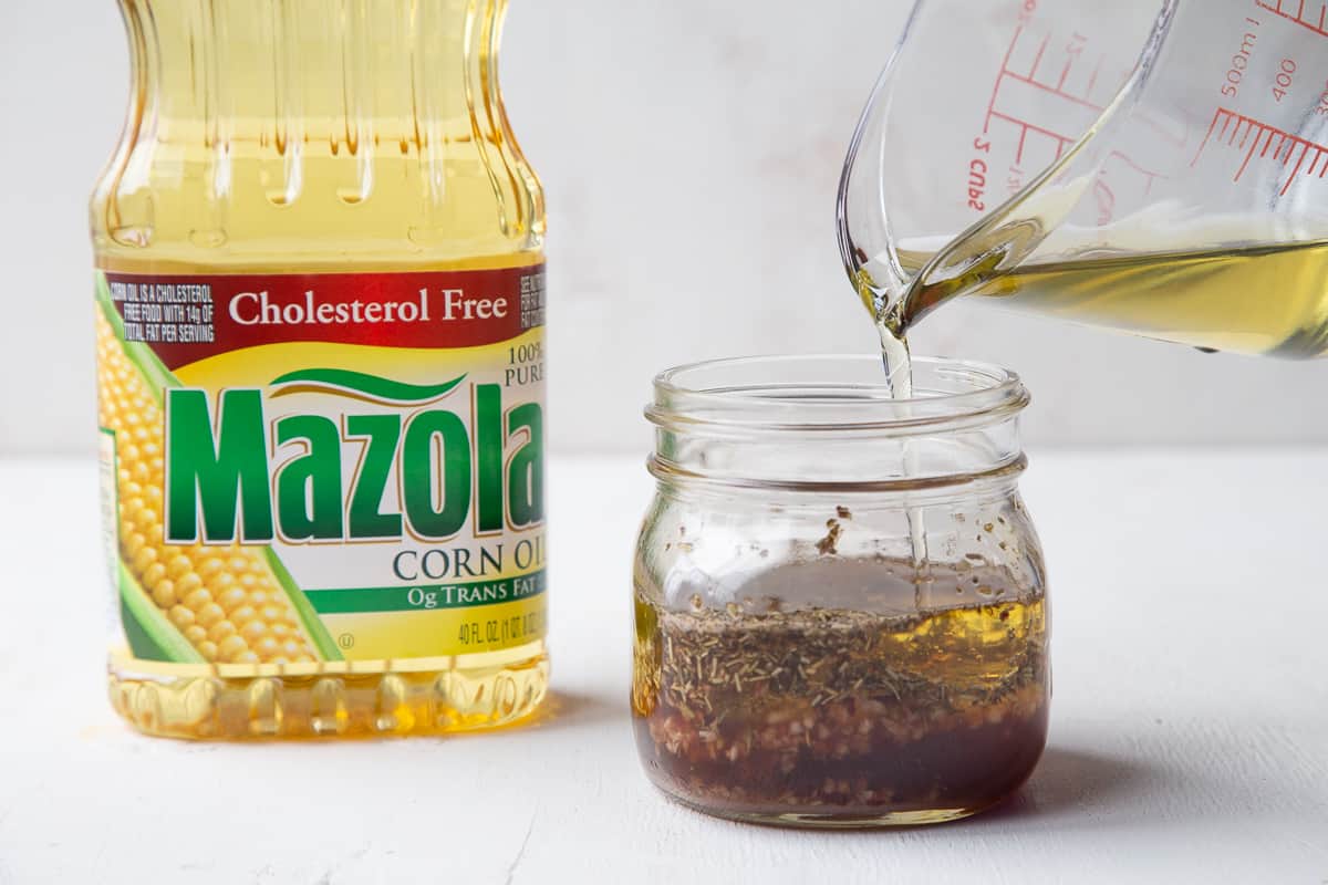 measuring glass pouring oil into a mason jar full of vinaigrette.