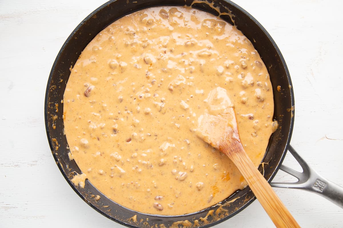 nacho cheese dip in a skillet with a wooden spoon.