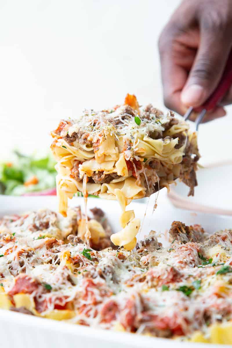 hand lifting up a scoop of pizza casserole from a white casserole dish.