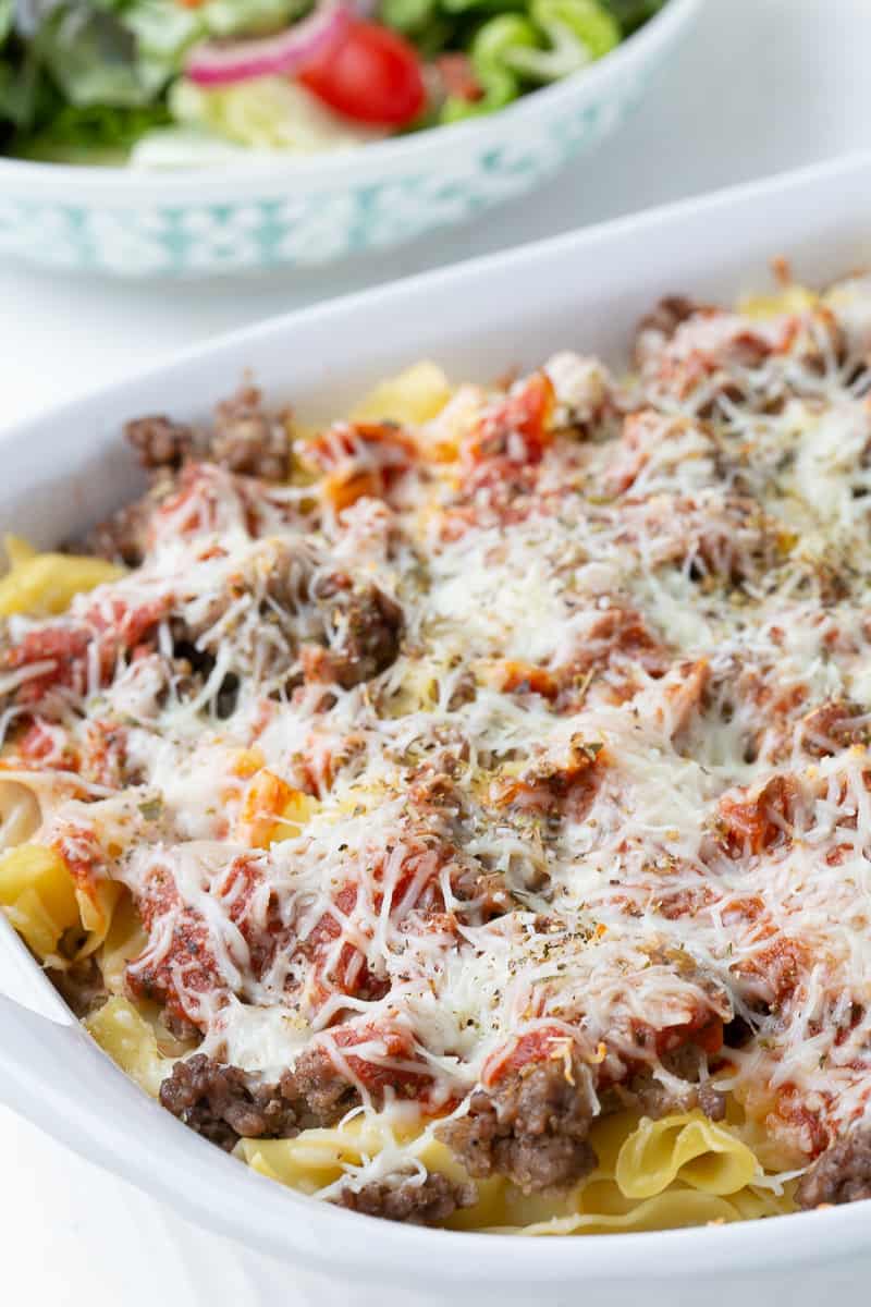 pizza casserole in a white dish with a green salad next to it.