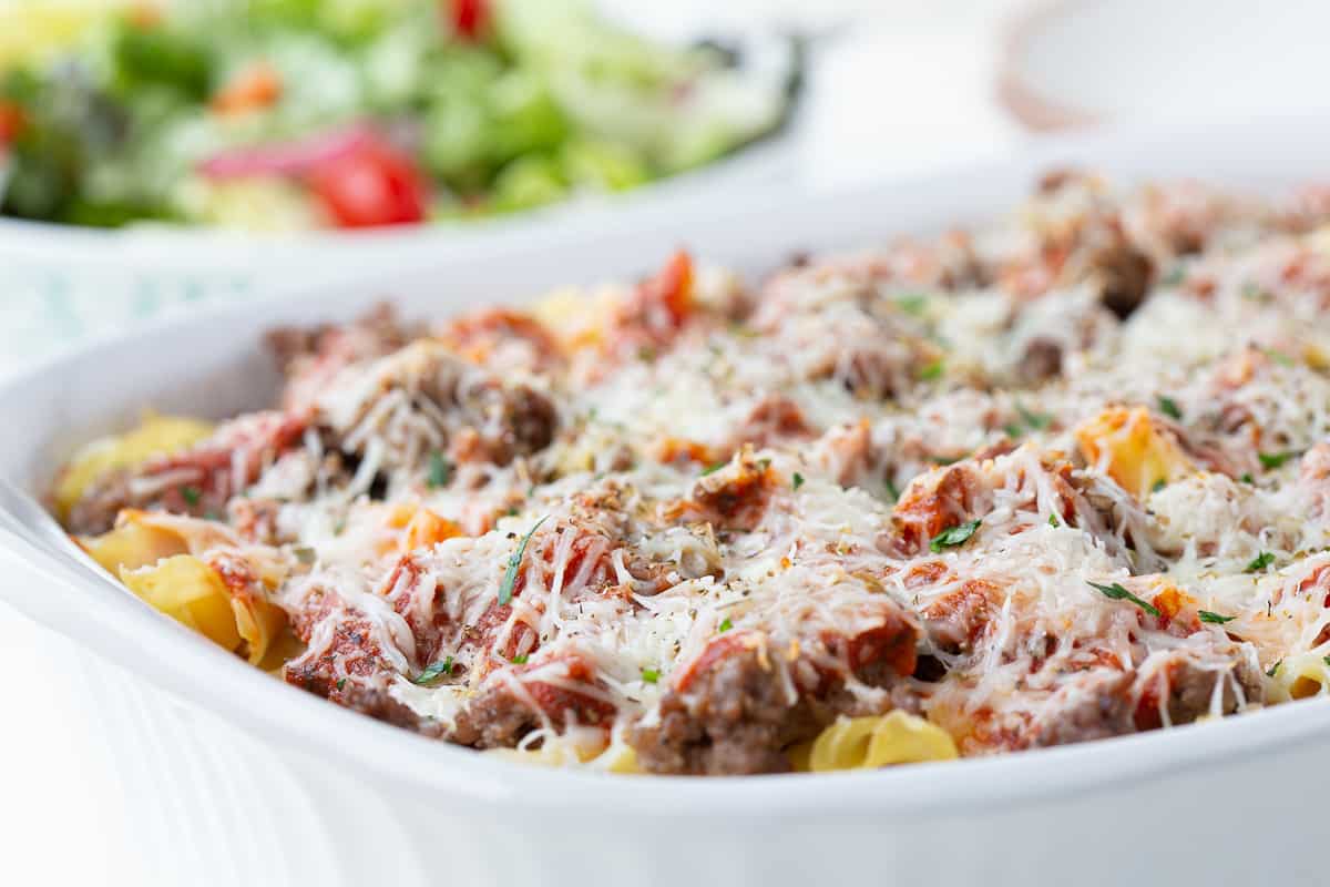 pizza casserole topped with cheese with a leafy green salad in the background.