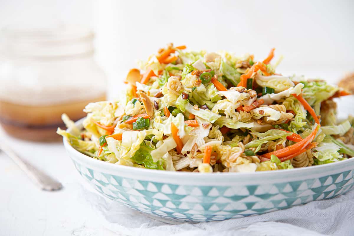 asian cabbage salad in a decorative bowl next to a glass jar of asian dressing.