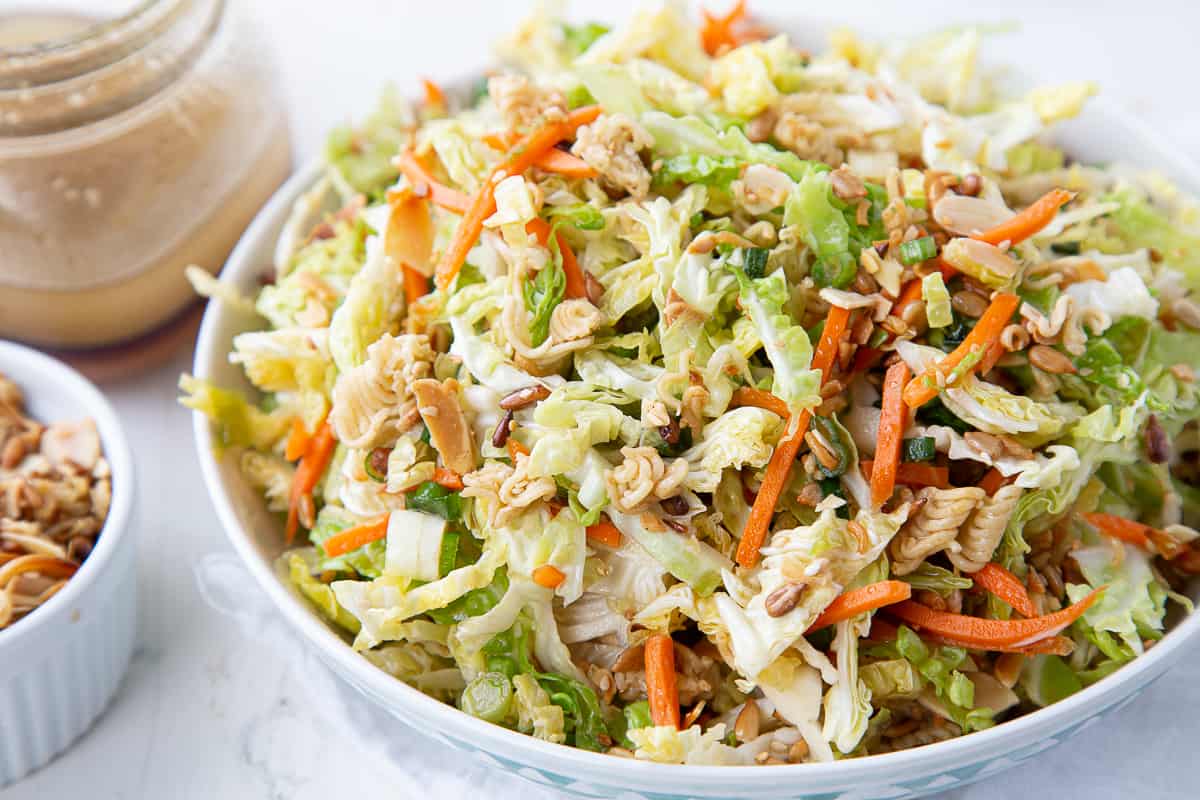 white bowl filled with asian cabbage salad next to a glass jar of dressing.