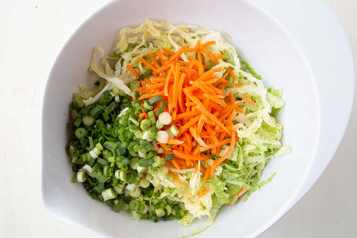 cabbage, carrots, and green onions in a large white bowl.