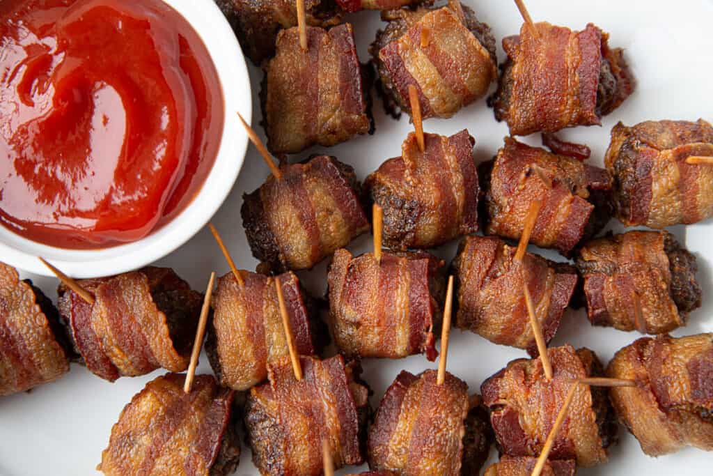 bacon wrapped meatballs on a white platter with a small bowl of ketchup.