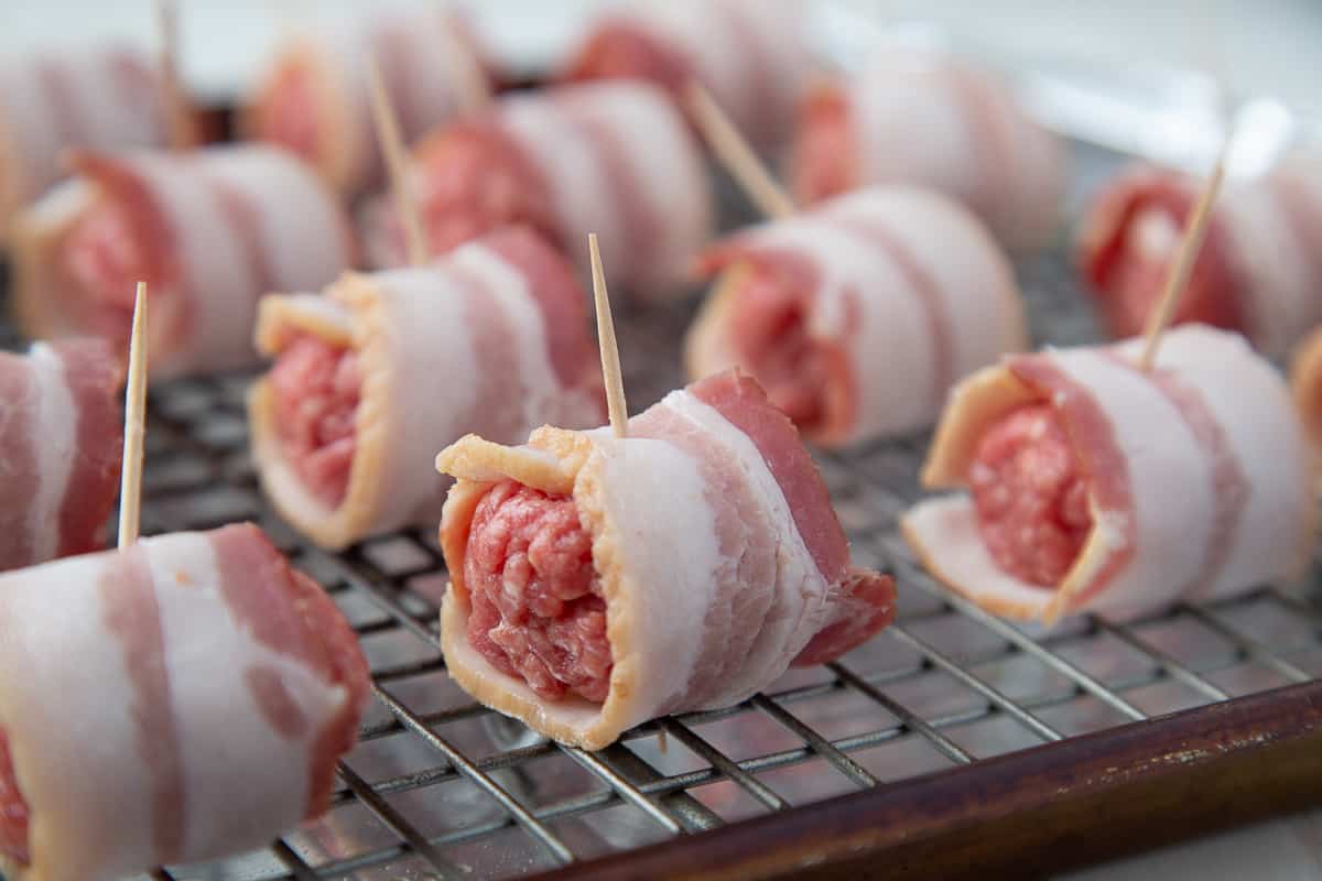 bacon wrapped around meatballs, secured with toothpicks on a baking sheet lined with a wire rack.