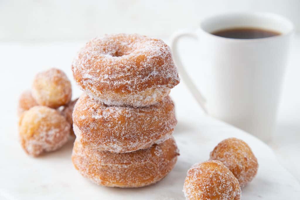stack of biscuit donuts and donut holes next to a white mug of coffee.