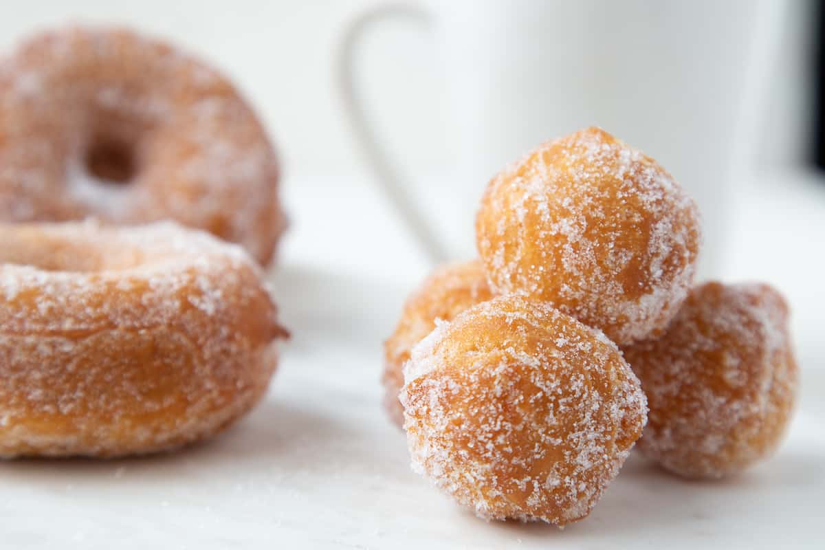 sugared donut holes next to whole donuts with a white mug of coffee.