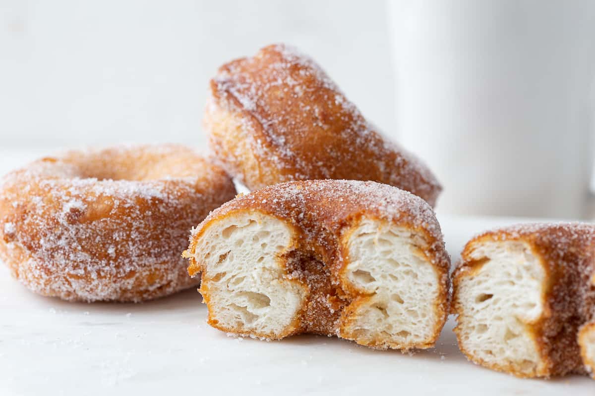 biscuit donut cut in half crosswise to show layers, next to whole donuts on a white table.