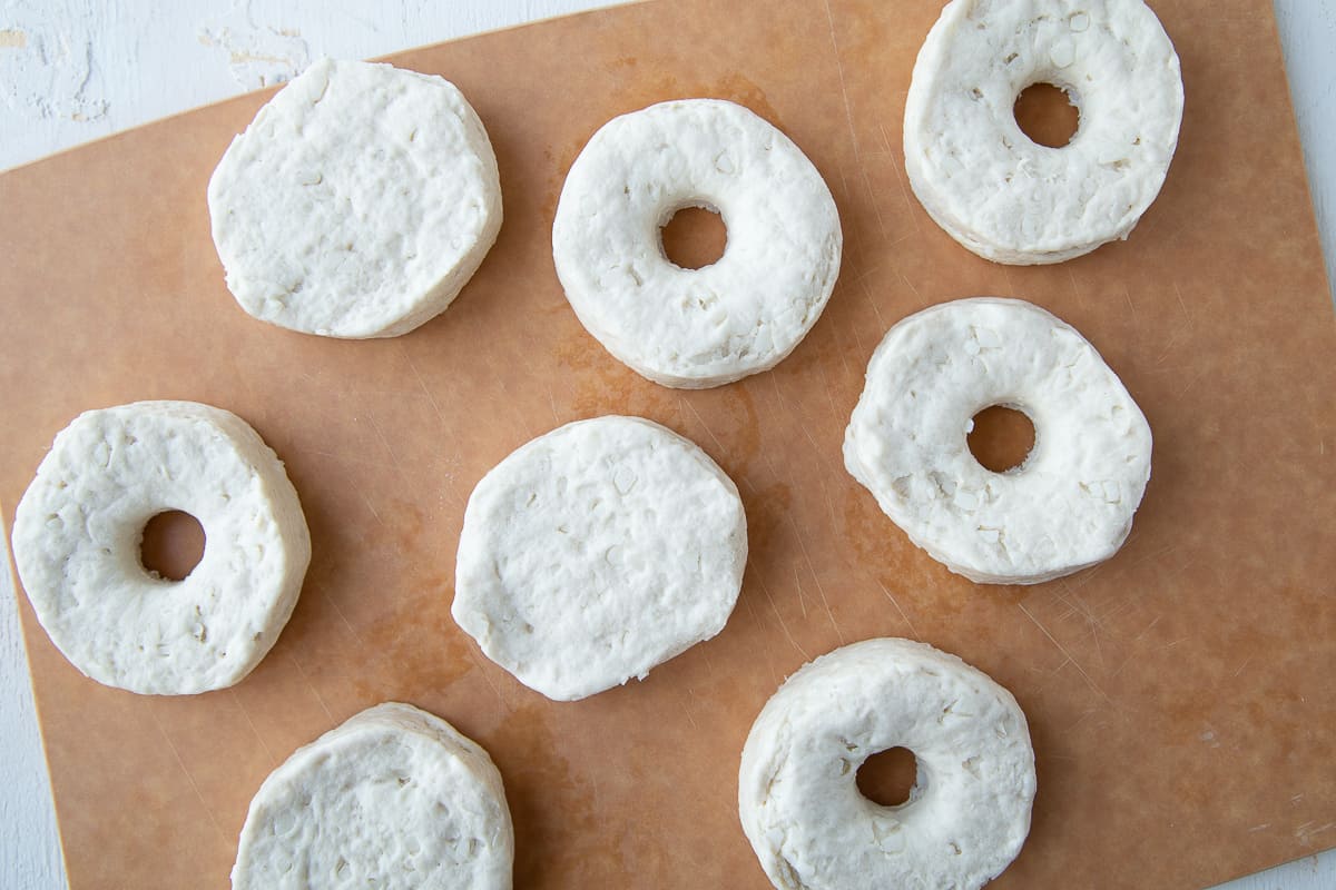 biscuit dough on a cutting board, cut into donut shapes.