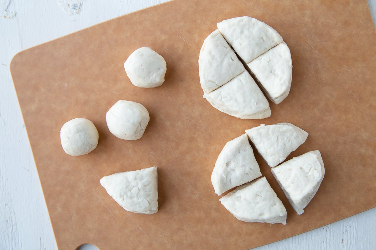 balls of biscuit dough forming donut holes on a wooden cutting board.