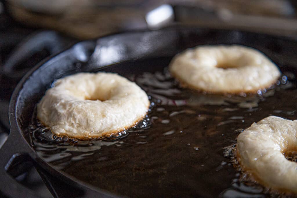 raw donuts frying in hot oil in a cast iron pan.