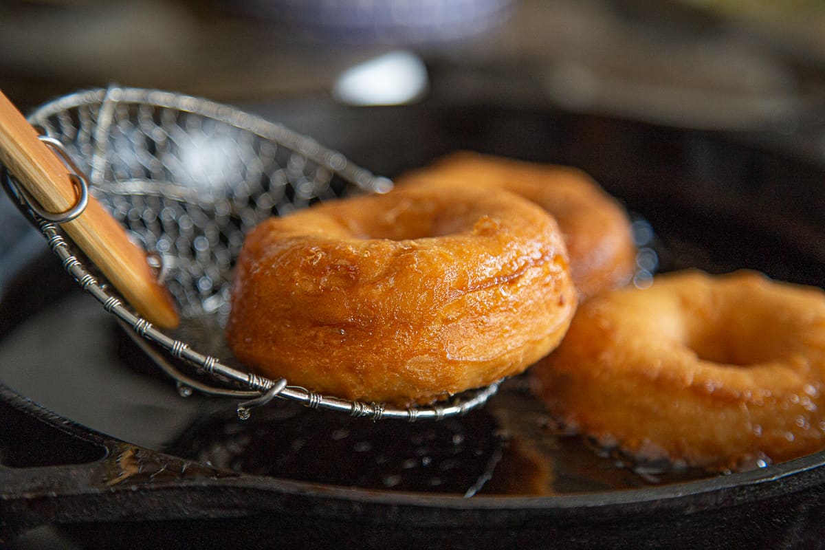 spider tool lifting a donut out of hot oil in a cast iron pan.