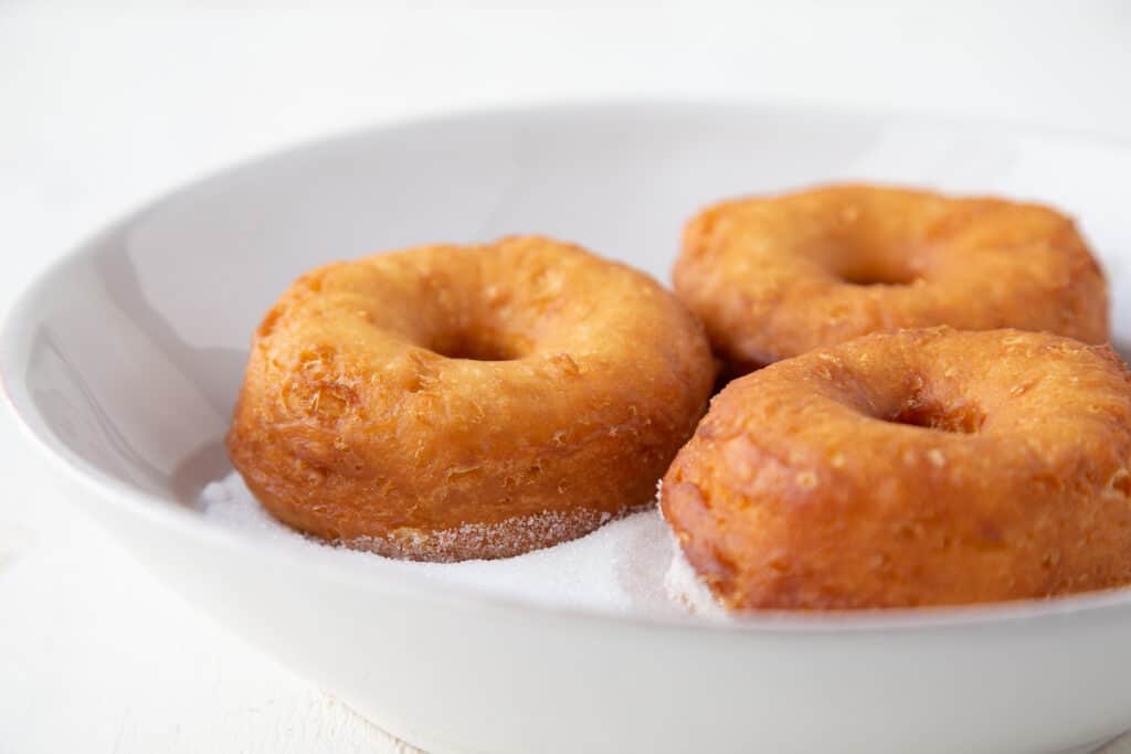 hot donuts in a white shallow bowl with granulated sugar.